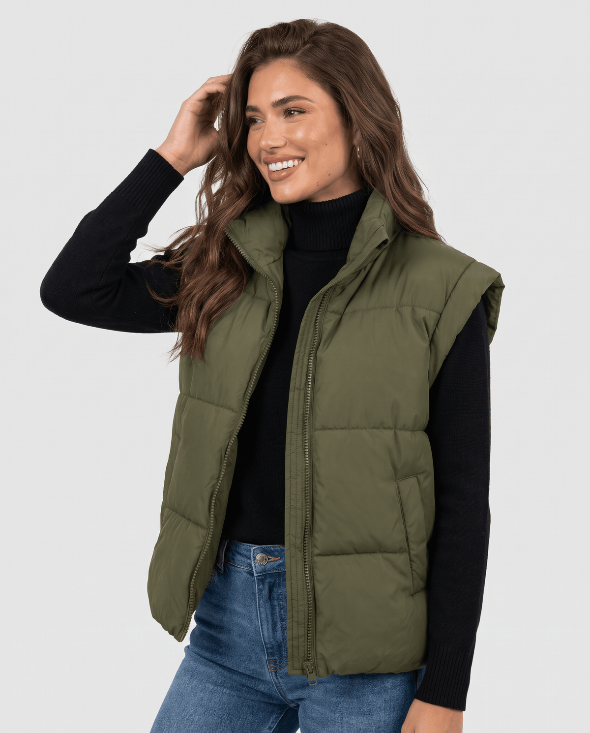 Green padded stand collar vest zipped over a black top and blue jeans