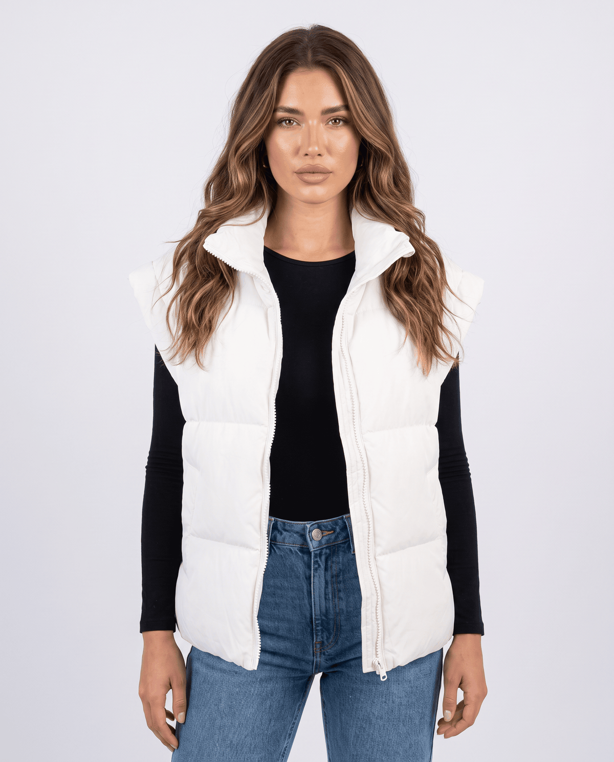 White padded stand collar vest zipped over a black top and blue jeans