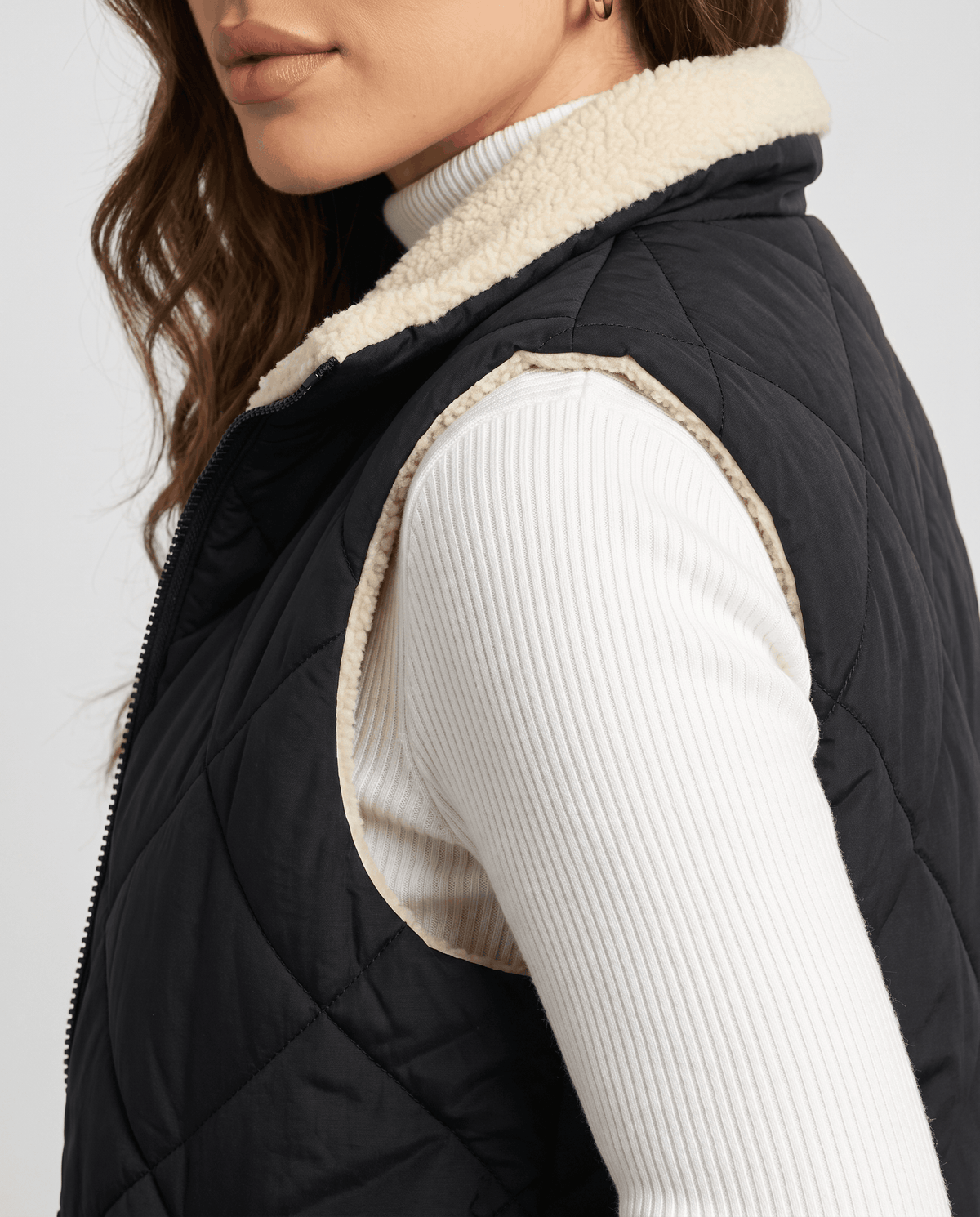 Close side view of black quilted vest cream sherpa lining and quilting