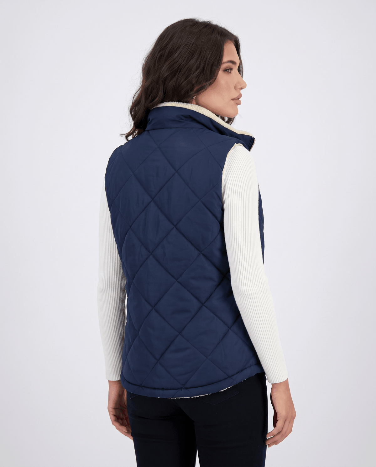 Back view of blue diamond-quilted sleeveless vest worn with a turtleneck