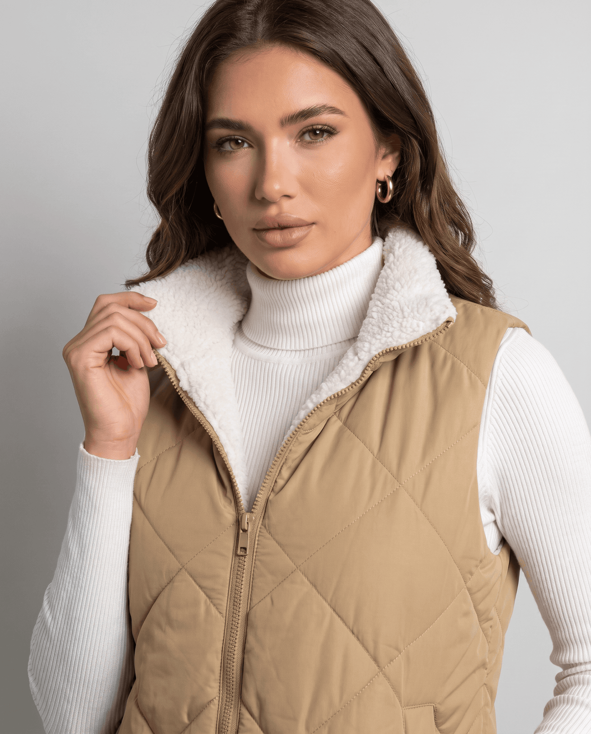 Model holding the collar of a khaki quilted vest with zip closed