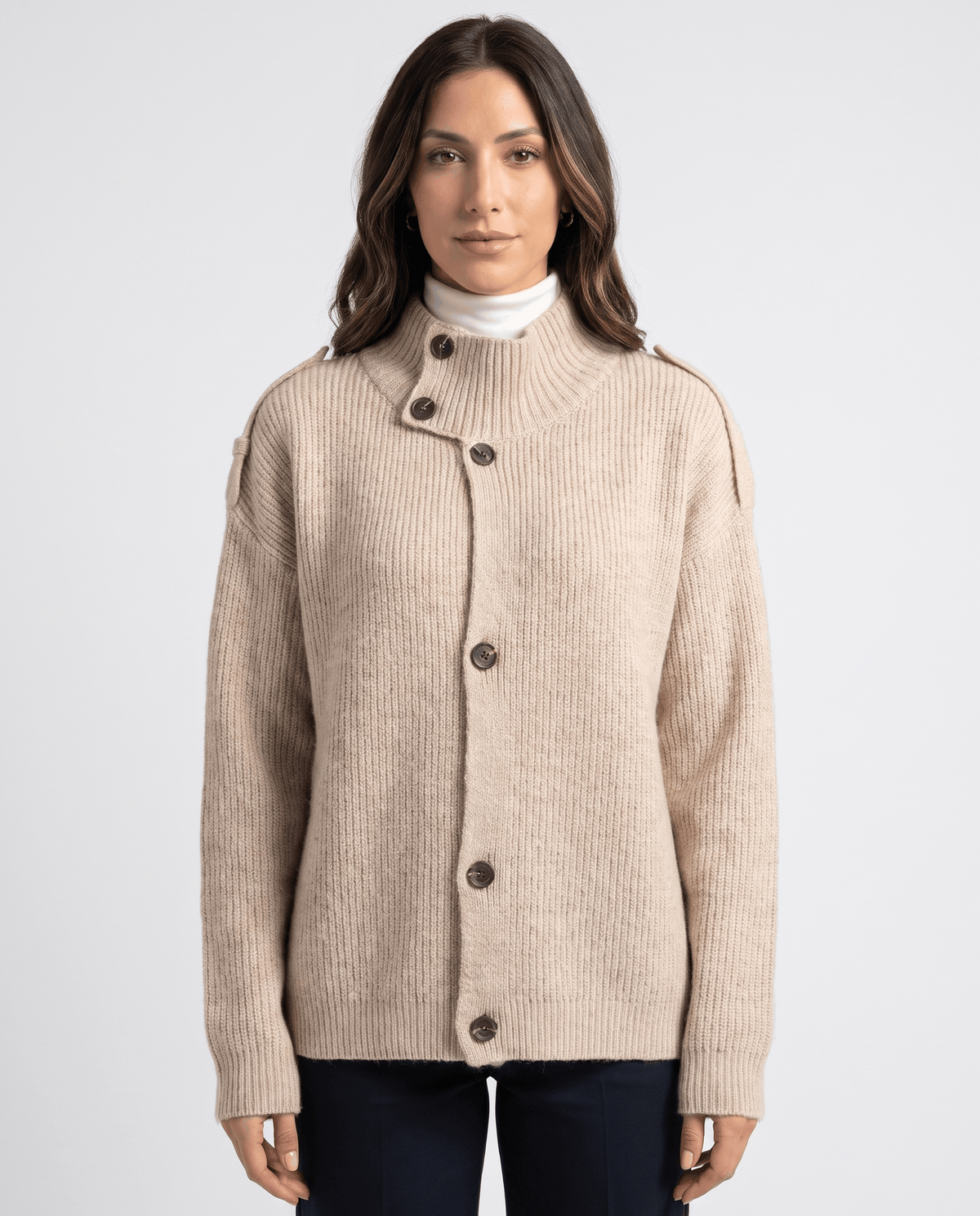 Woman wearing light beige ribbed knit cardigan with stand collar and button front over a white turtleneck