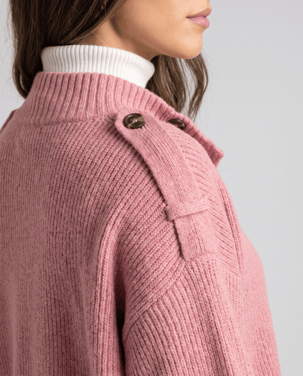 Close-up of pink ribbed knit cardigan shoulder strap button and stand collar detail