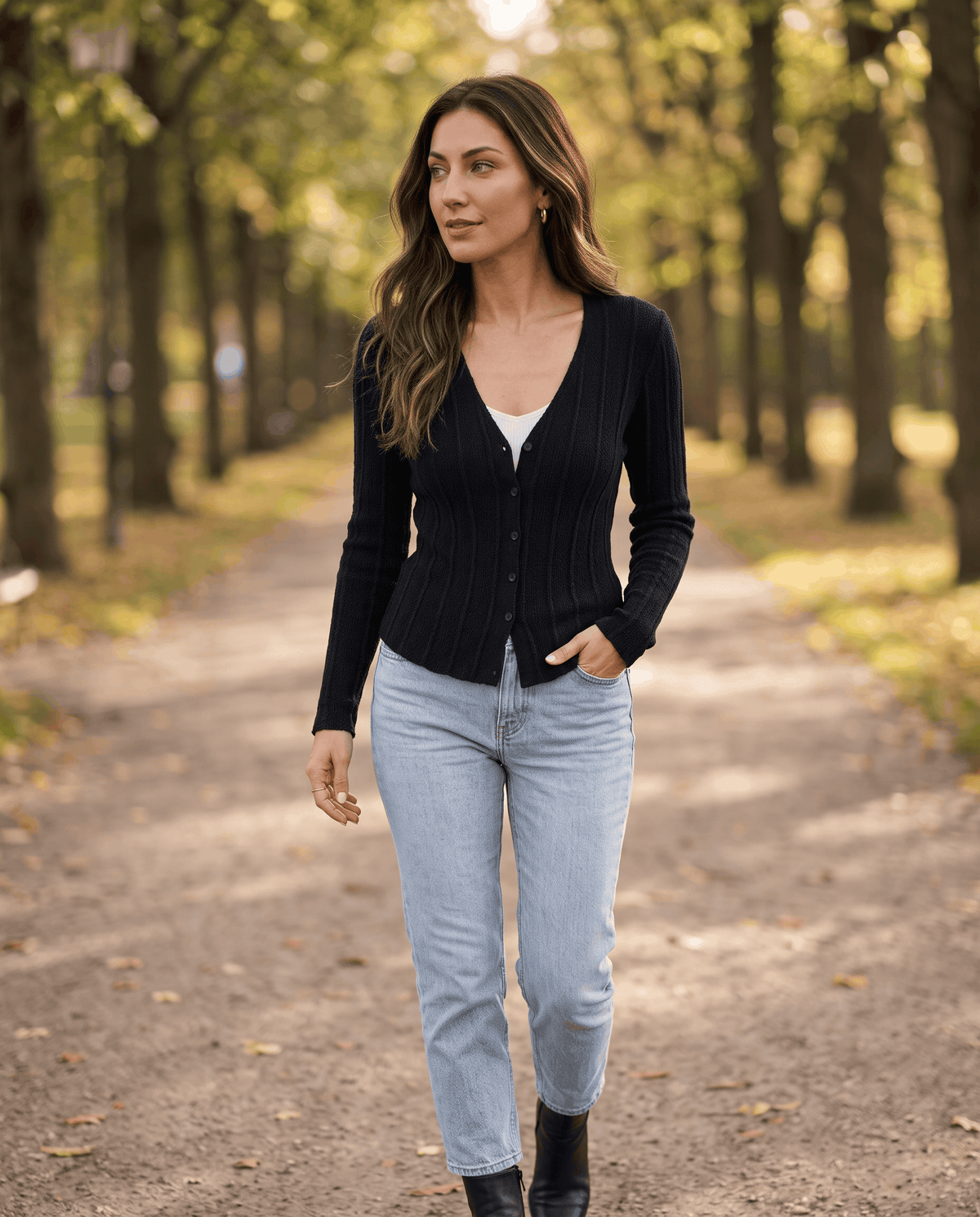 Woman walking in a black ribbed button-front cardigan and light blue jeans along a tree-lined path
