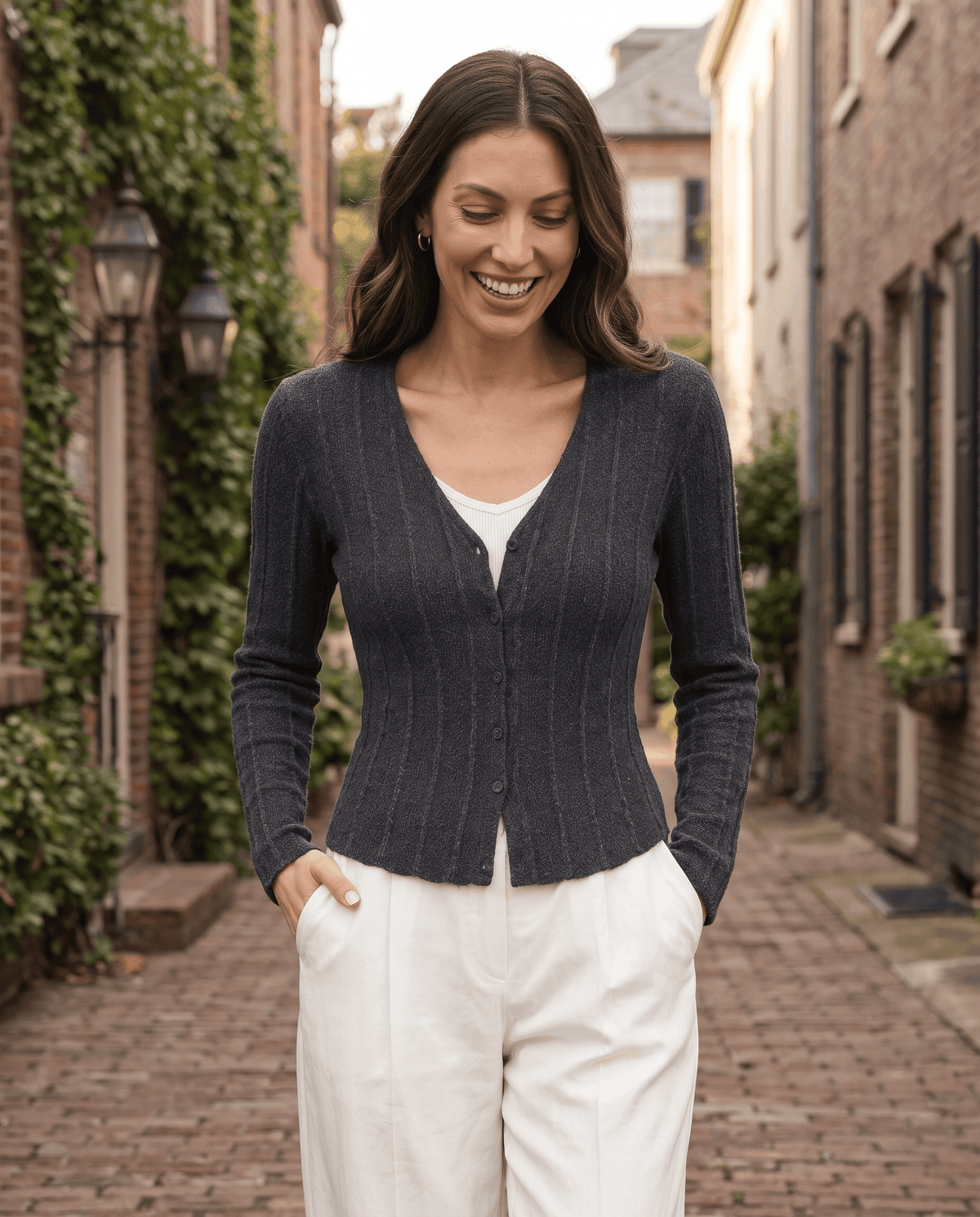 Woman walking in a dark gray ribbed button-front cardigan and cream trousers on a brick street