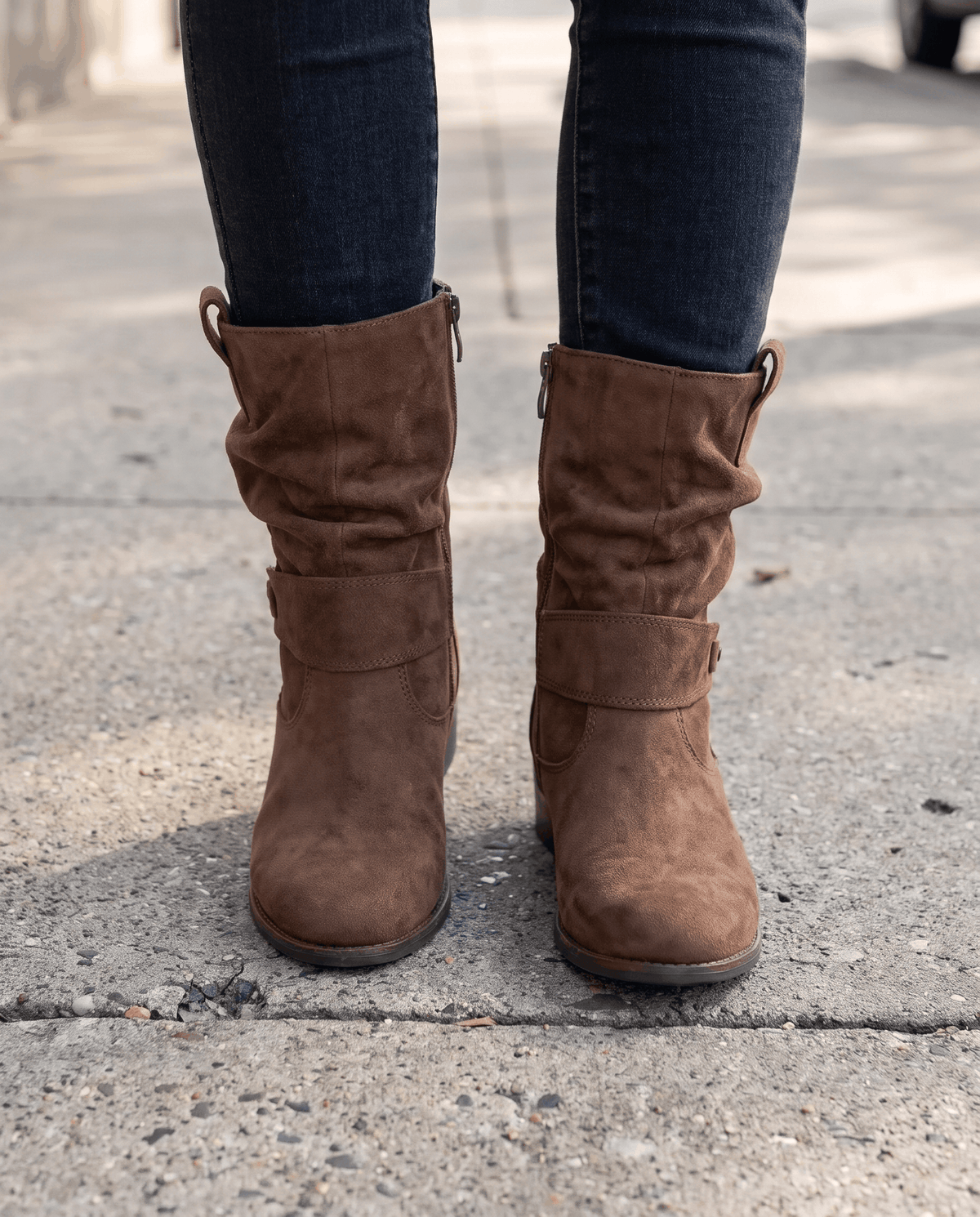Brown suede slouch boots worn with dark jeans on pavement