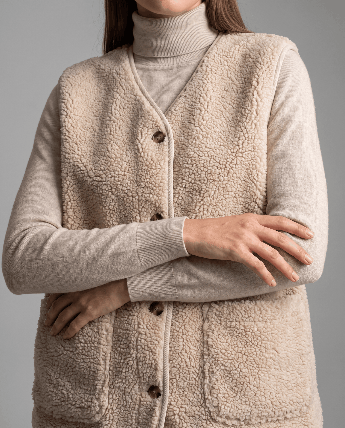 Close-up of beige teddy fleece vest with arms crossed, showing buttons and patch pocket