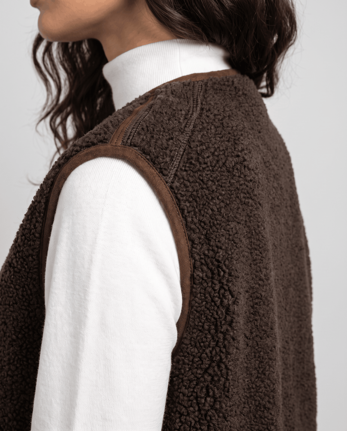 Side close-up of brown teddy fleece vest showing the curly texture and armhole