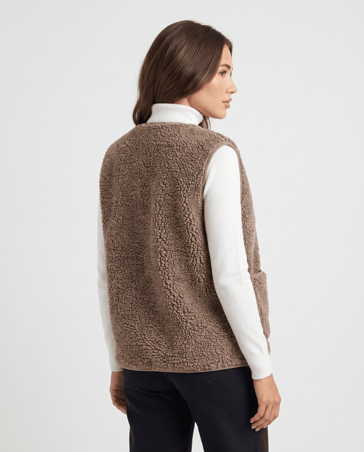 Back view of taupe teddy fleece vest over a white turtleneck and dark trousers