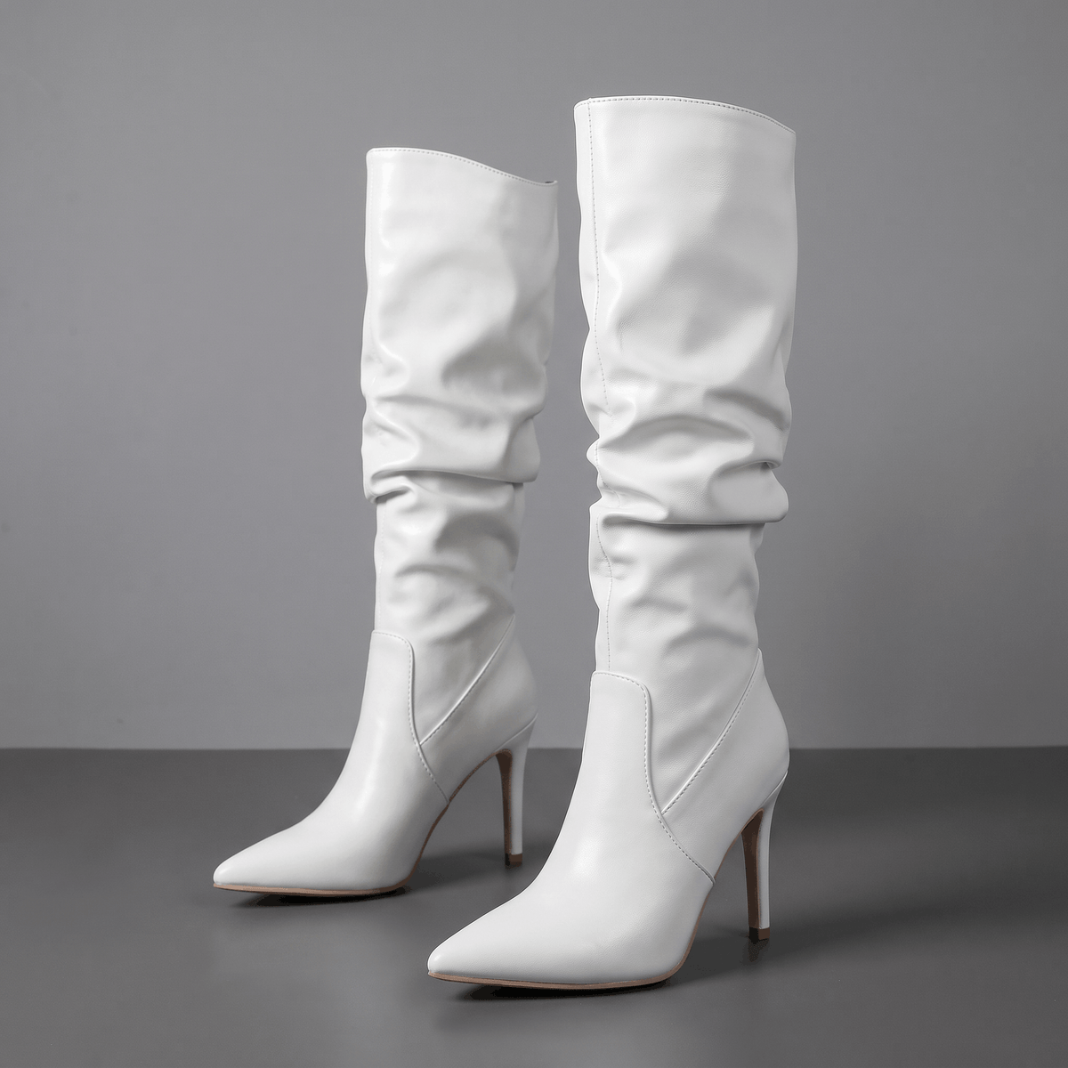 White vegan leather knee-high boots with a ruched slouch shaft, pointed toe, and slim stiletto heel.