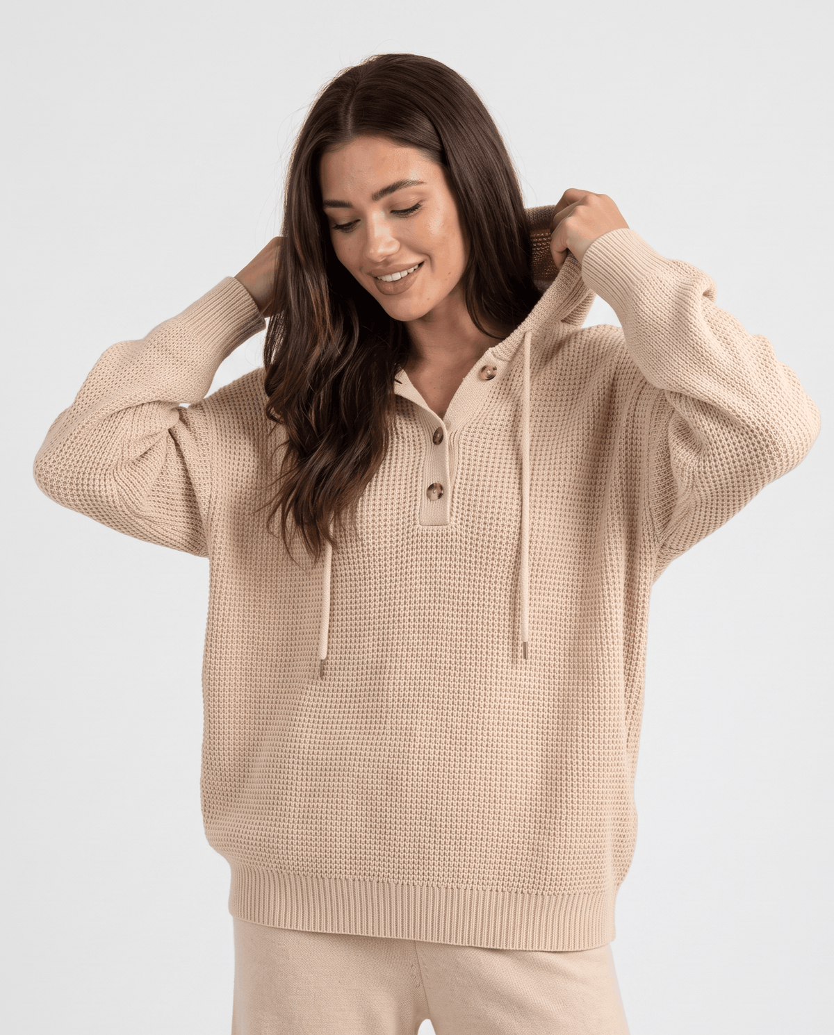 Beige waffle knit hoodie worn with a hand at the hood, front view