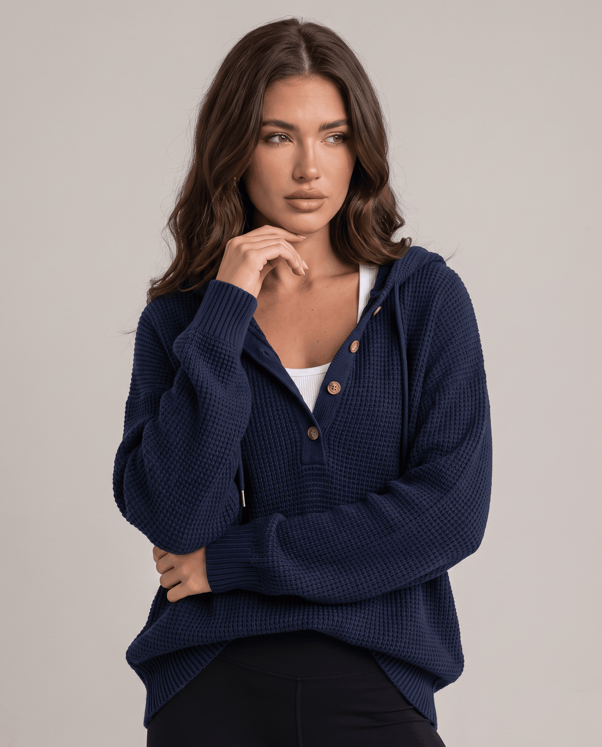 Navy waffle knit hoodie with buttoned neckline layered over a white top, hand at the chin