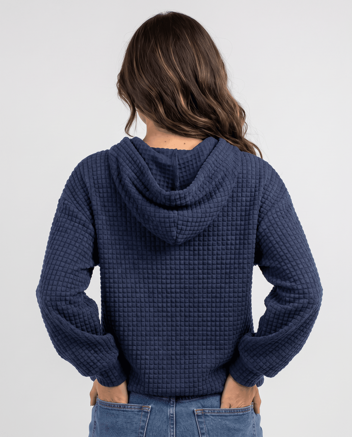 Back of navy blue hoodie with the hood down and hands in pockets