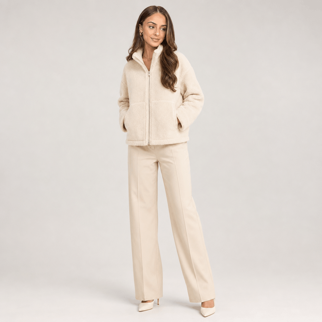 Full-body view of a female model wearing the cream sherpa jacket with matching light-colored trousers.