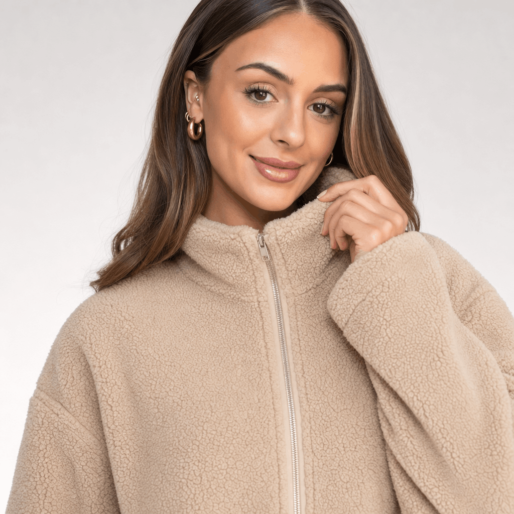 Close-up of the female model wearing the light beige sherpa jacket, highlighting the soft textured fabric, full-length zipper, and stand collar.