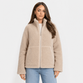 Female model wearing a light beige sherpa zip-up jacket with a high stand collar and large front patch pockets, paired with blue jeans.