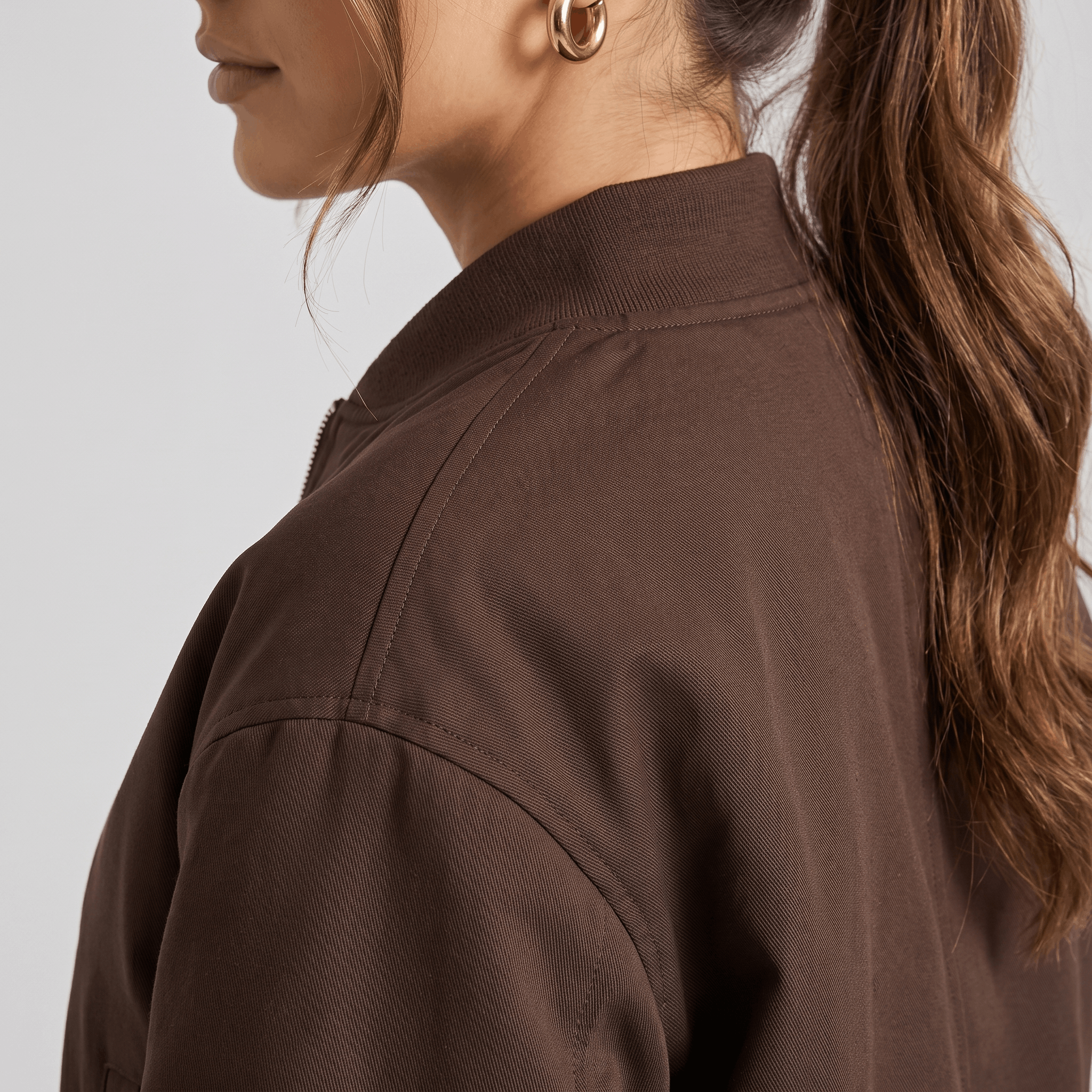 Detailed view of the dark brown bomber jacket, highlighting the stand collar, zipper, and smooth fabric.