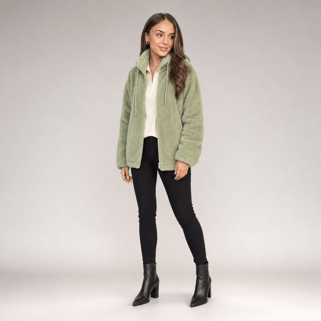 Full-body view of a female model wearing the light green sherpa fleece jacket with black trousers and ankle boots.