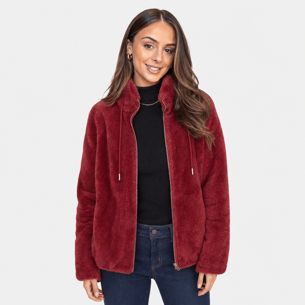 Female model wearing a deep red sherpa fleece zip-up jacket over a black top, paired with blue jeans.