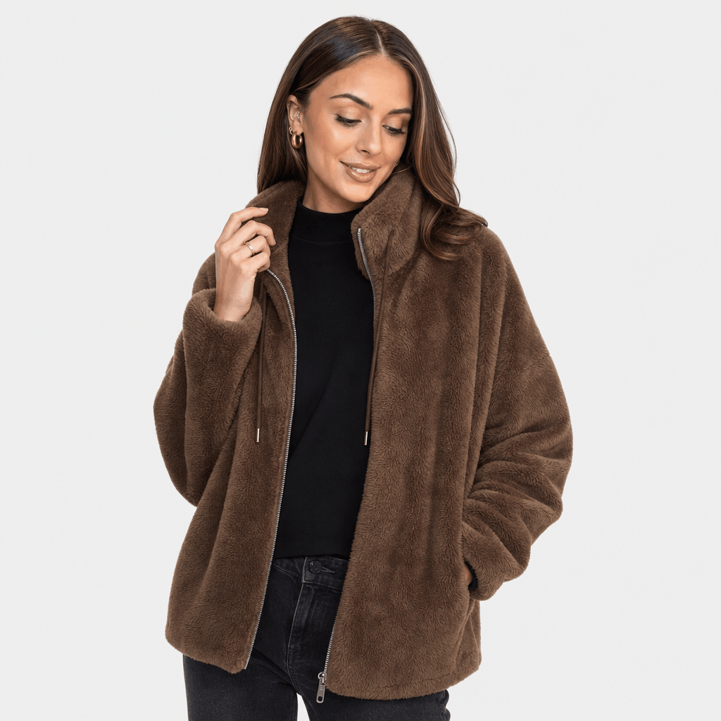 Female model wearing a brown sherpa fleece zip-up jacket with a high collar, paired with a black top and black trousers.