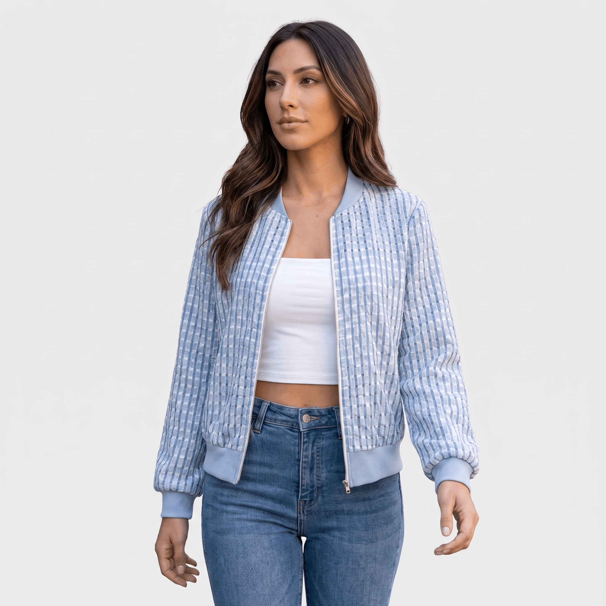 Female model wearing a light blue textured zip-up jacket over a white crop top, paired with blue jeans.