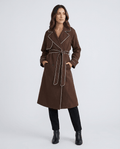 Brown belted trench coat for women with a defined waist, contrast stitching, tie belt, double-breasted front, and lapel collar