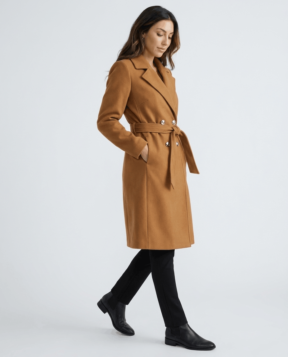 A woman wearing a brown belted wool trench coat with a tailored fit, lapel collar, and long sleeves, side view