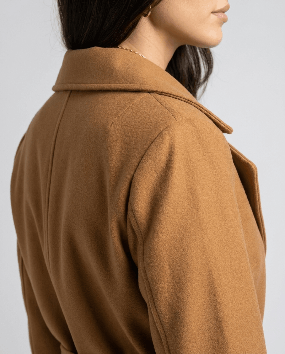 Close-up of a woman wearing a brown belted wool trench coat, showing the back collar and wool texture