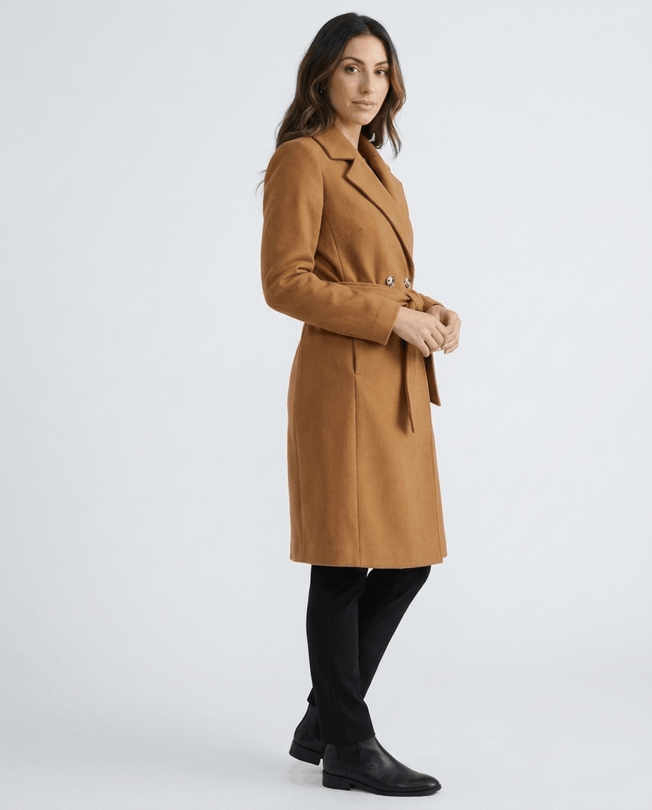 A woman wearing a brown belted wool trench coat with a tailored fit, shown in a side view