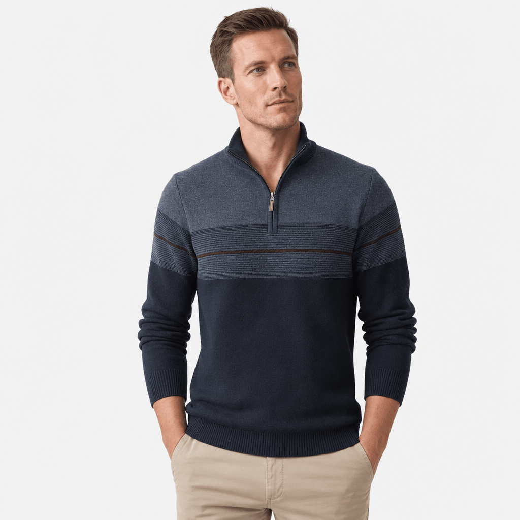 Man wearing a navy blue quarter-zip sweater with a textured gray upper panel and thin horizontal stripe detail, paired with beige pants.