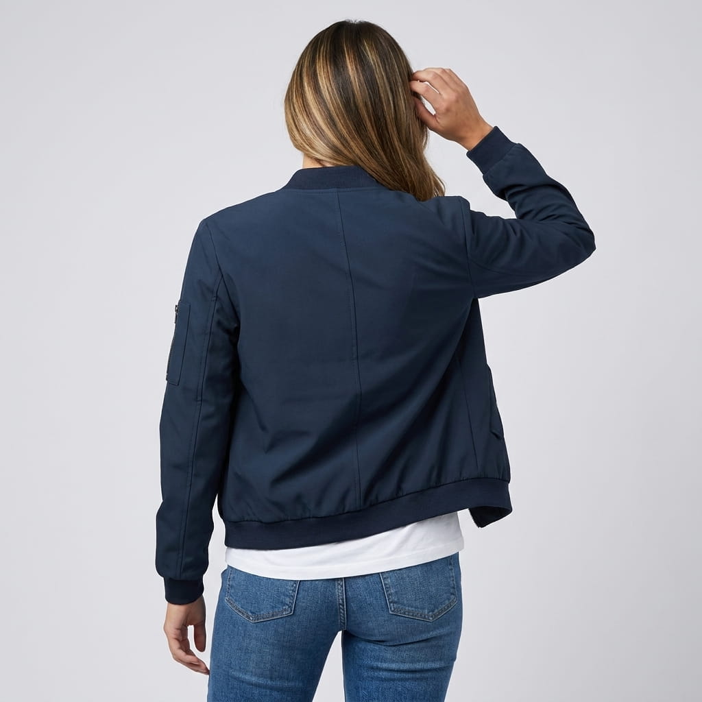 Female model wearing a navy blue bomber jacket with a ribbed collar, cuffs, and hem, paired with blue jeans.