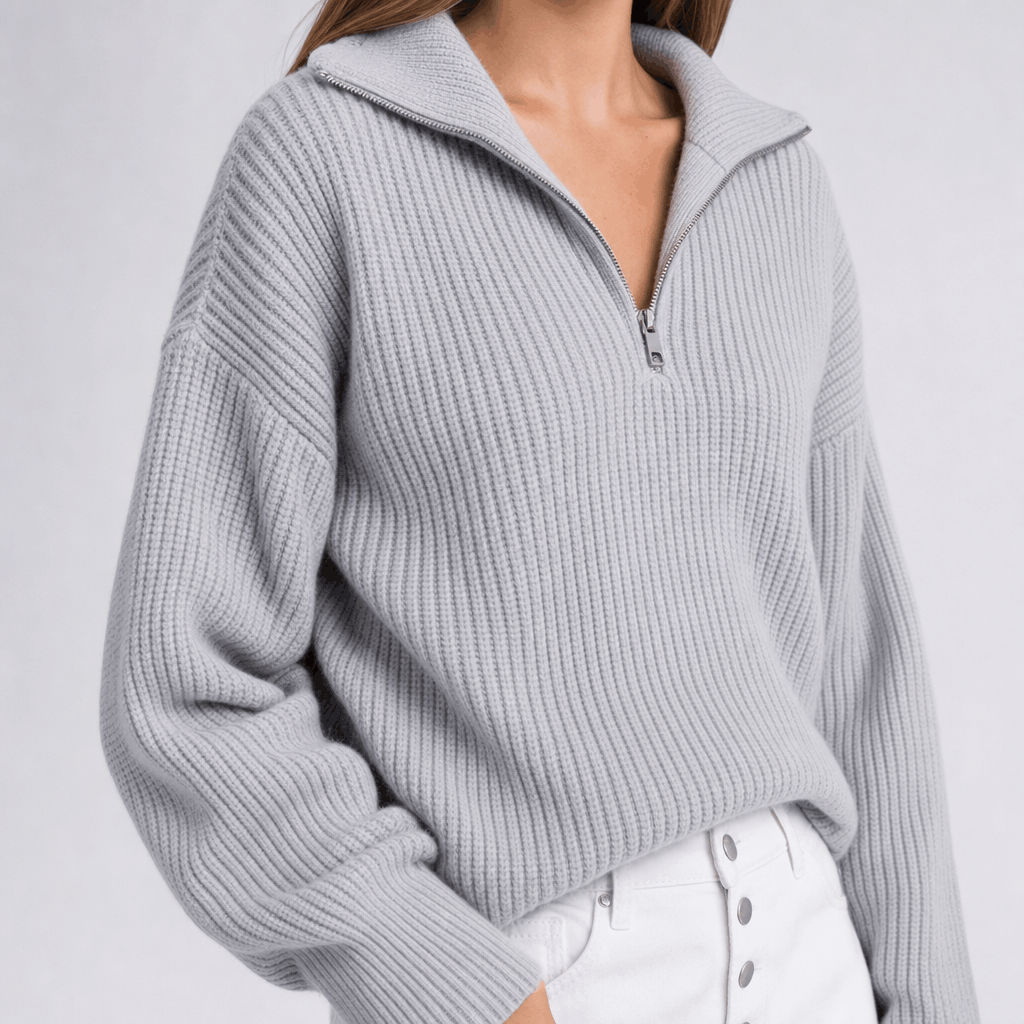 Close-up showing the light gray ribbed half-zip sweater with a relaxed folded collar and white pants.