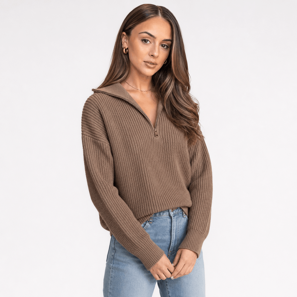 Woman wearing a taupe brown ribbed half-zip sweater with blue jeans, shown in a relaxed pose.