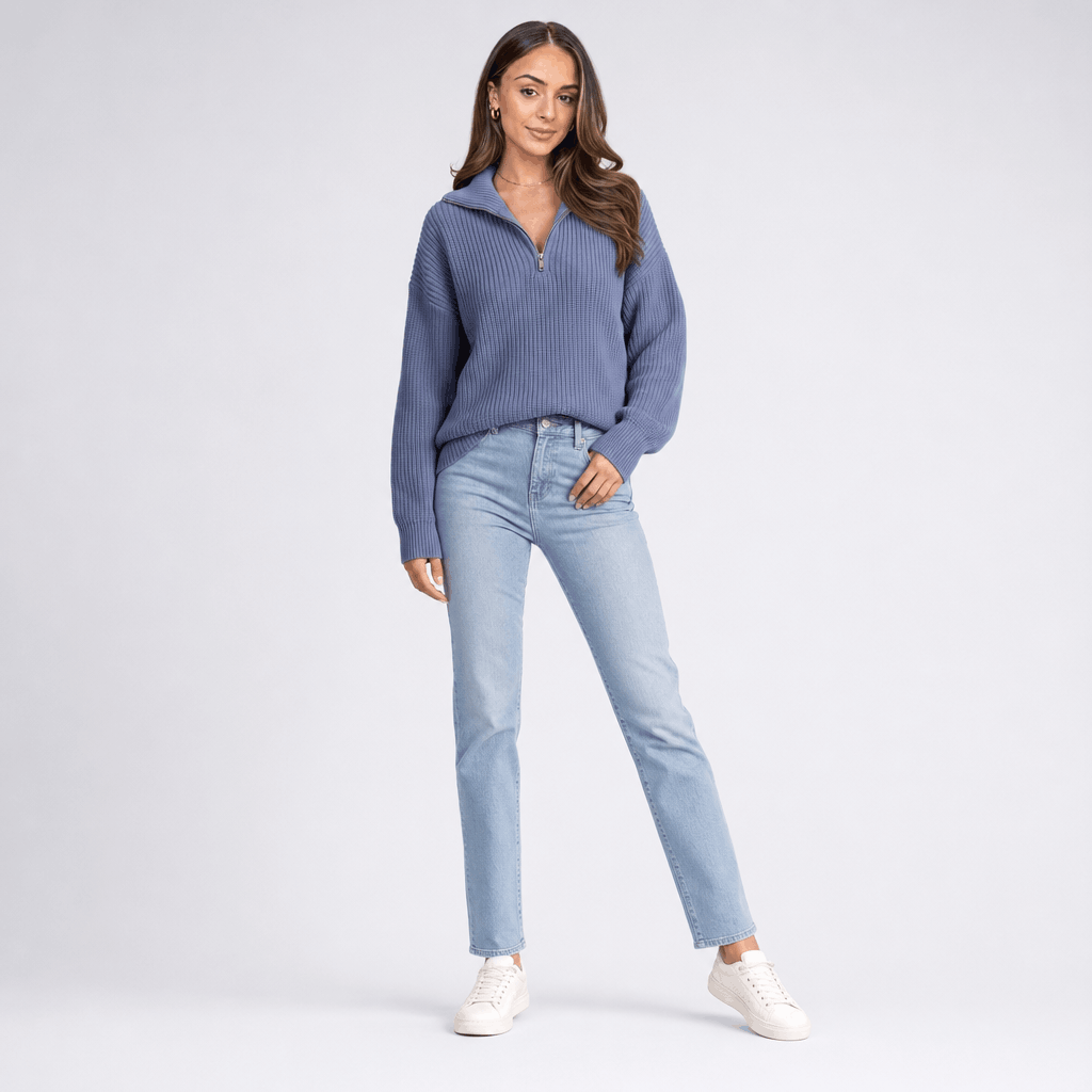 Full-body view of the woman wearing the slate blue half-zip sweater with light blue jeans.