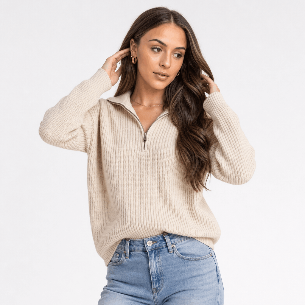 Woman wearing a cream ribbed half-zip sweater with blue jeans, shown touching her hair.