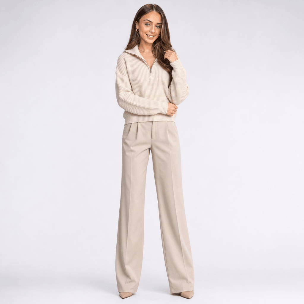 Full-body view of the woman wearing the cream half-zip sweater with matching light-colored pants.