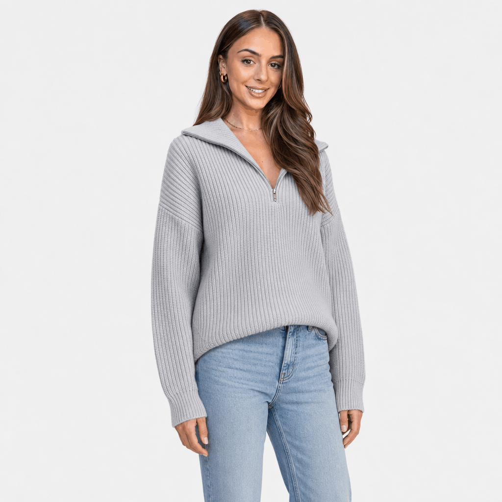 Woman wearing a light gray ribbed half-zip sweater with blue jeans, shown in a relaxed standing pose.
