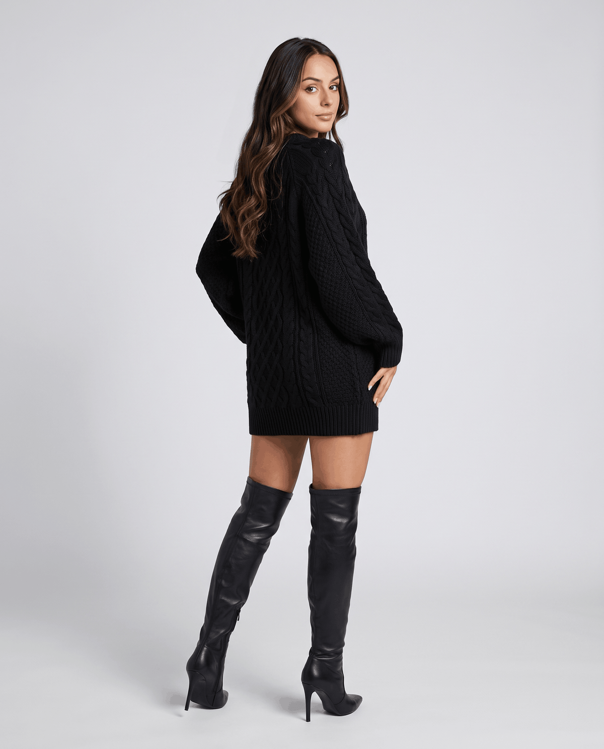 Black Cable Knit Sweater worn by a female model with a short skirt and knee-high boots, showcasing the oversized fit, cable knit texture, and balloon sleeves.