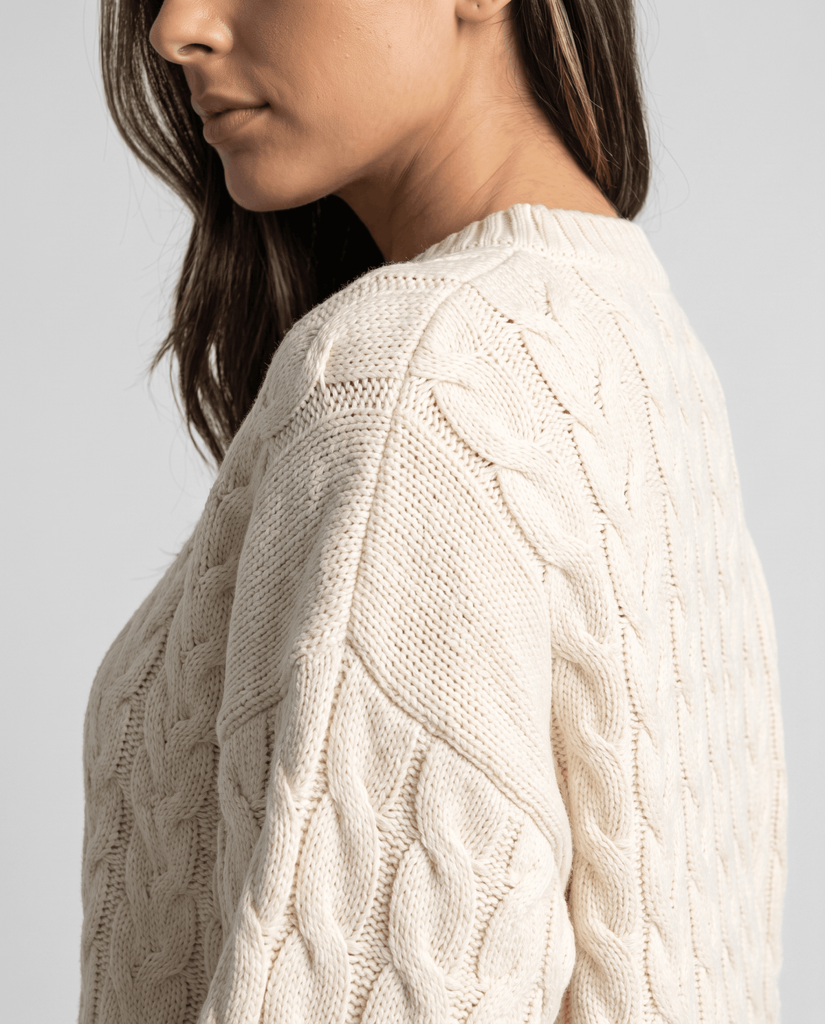 Cream Cable Knit Sweater worn by a female model from the side, showcasing the raised cable knit texture, relaxed oversized fit, and long sleeves.