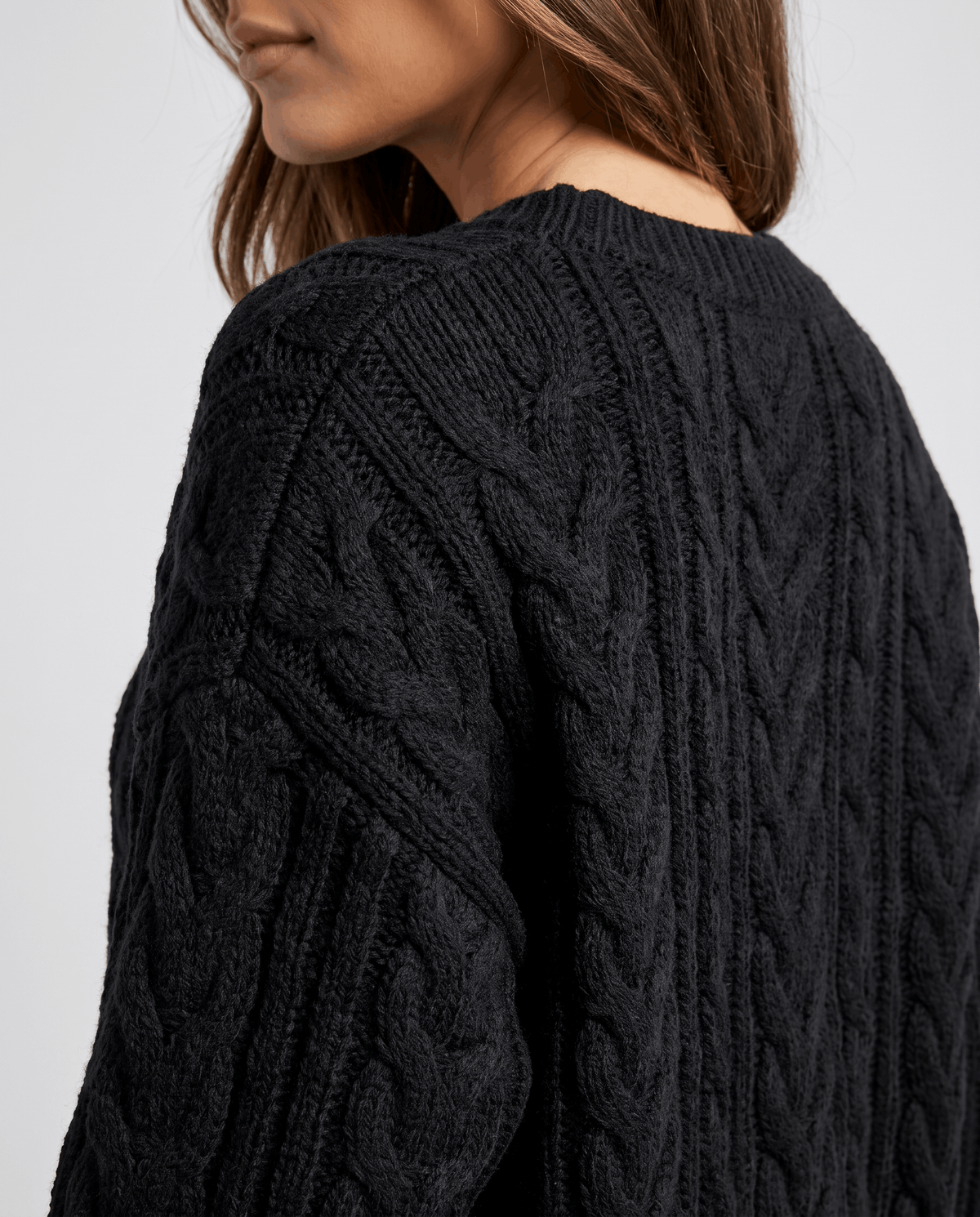 Black Cable Knit Sweater worn by a female model, shown in close-up from the back to highlight the textured cable knit pattern and oversized fit.