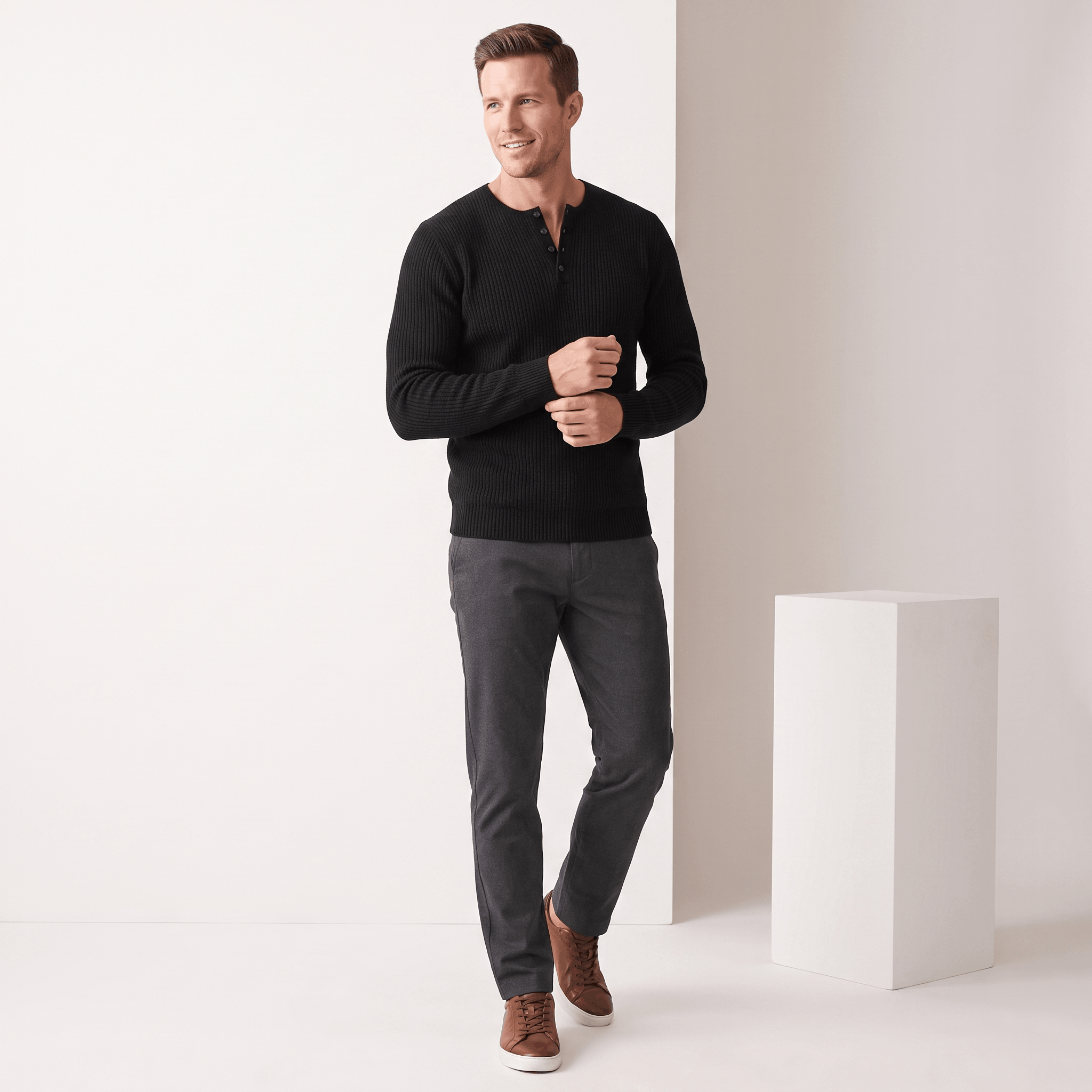 Black ribbed knit henley sweater with a four-button placket, worn in a regular fit with dark trousers and brown sneakers.