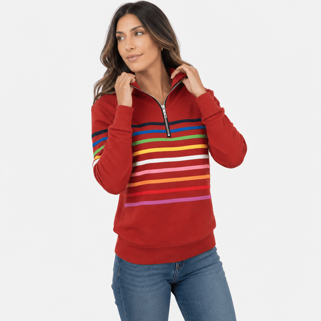 Female model wearing a red quarter-zip sweater with multicolored horizontal stripes across the chest and sleeves, paired with blue jeans.