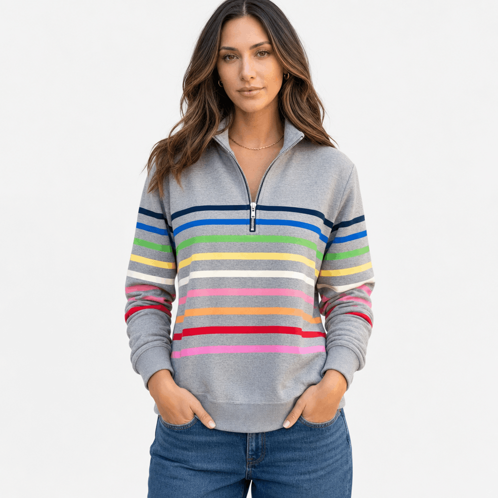 Female model wearing a gray quarter-zip sweater with multicolored horizontal stripes across the chest and sleeves, paired with blue jeans, front view.