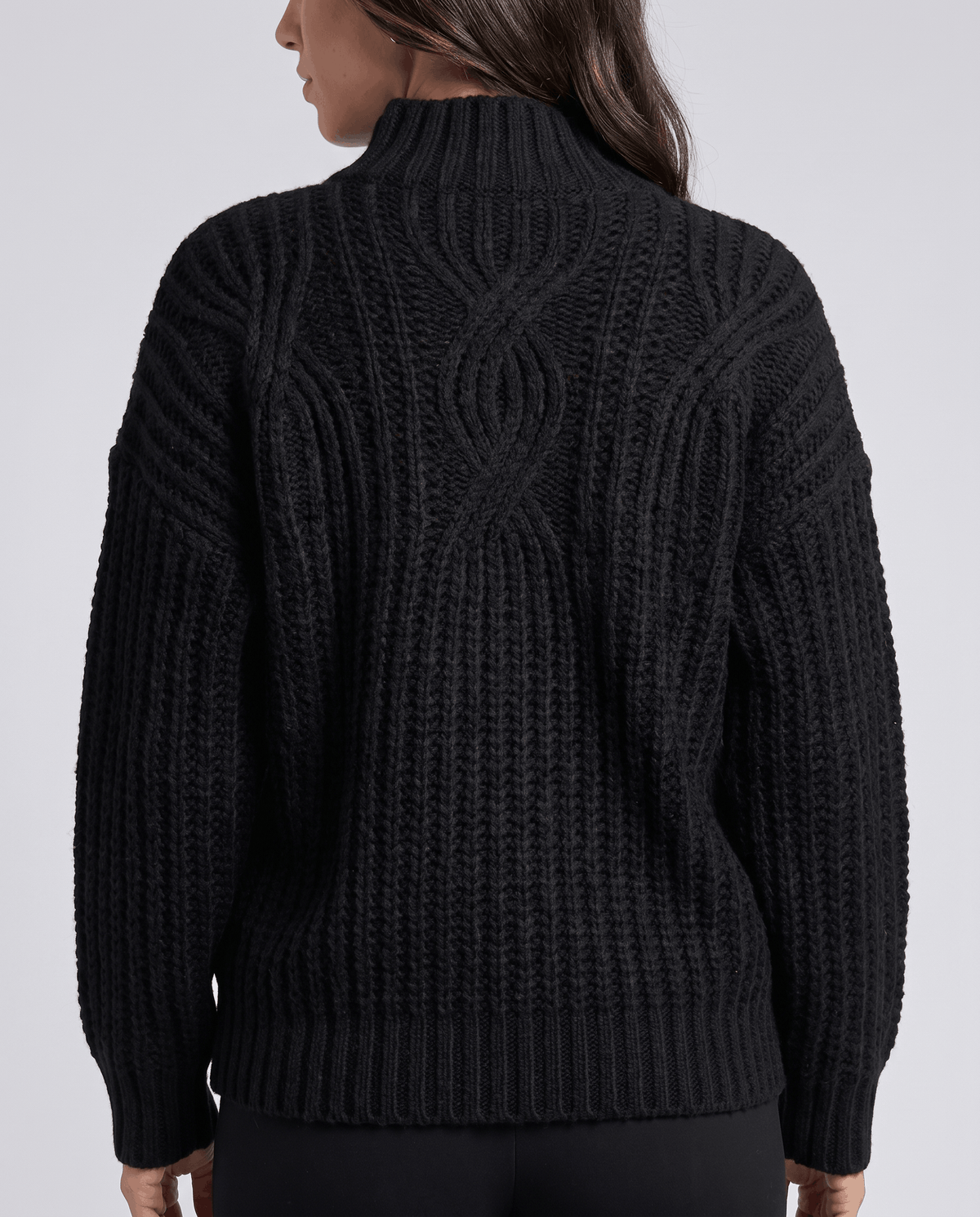Black Chunky Cable Knit Sweater worn by a female model from the back, showcasing the chunky cable knit texture, mock neck, relaxed fit, and ribbed hem.