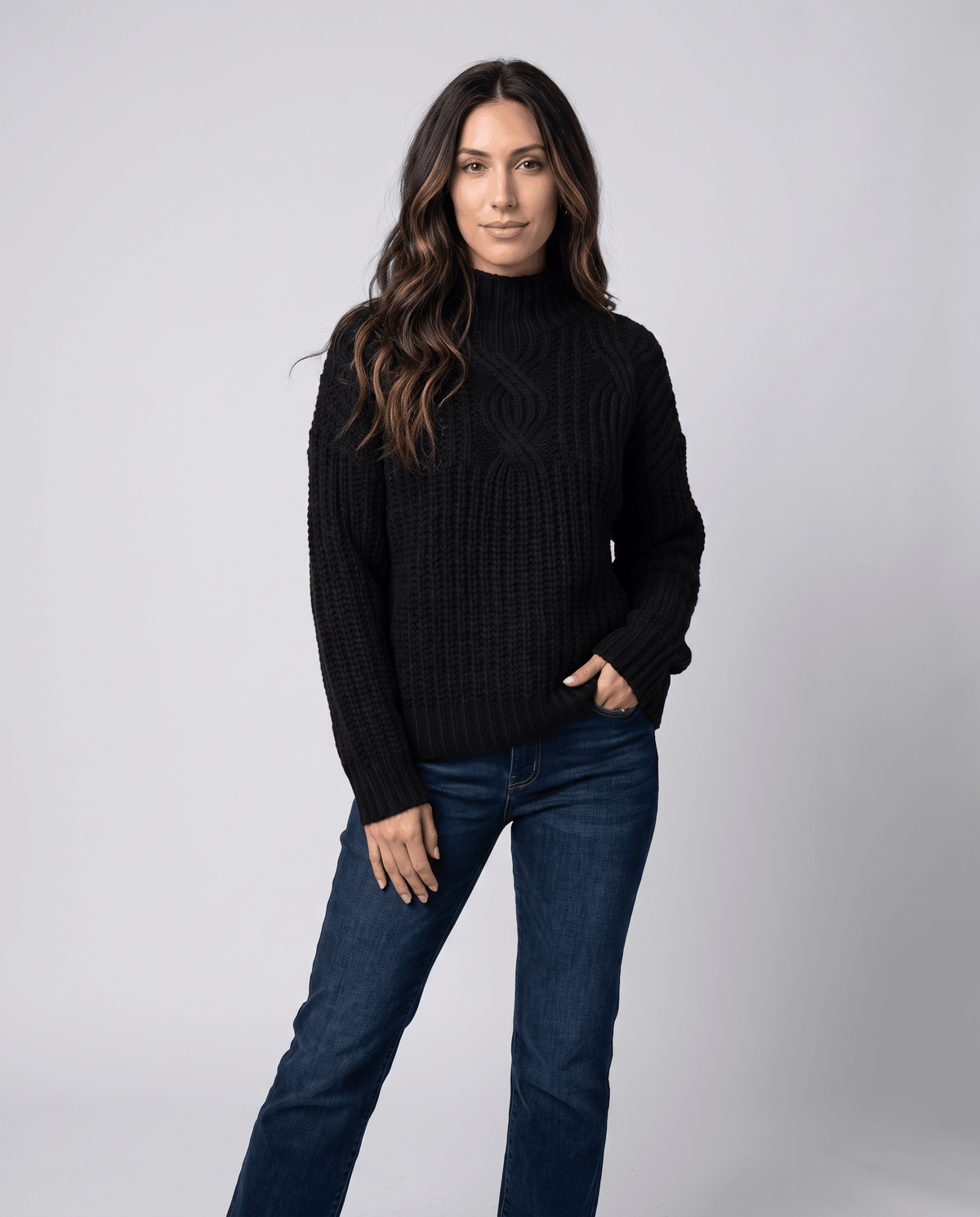 Black Chunky Cable Knit Sweater worn by a female model with blue jeans, featuring a mock neck, relaxed fit, chunky cable knit texture, and long sleeves.