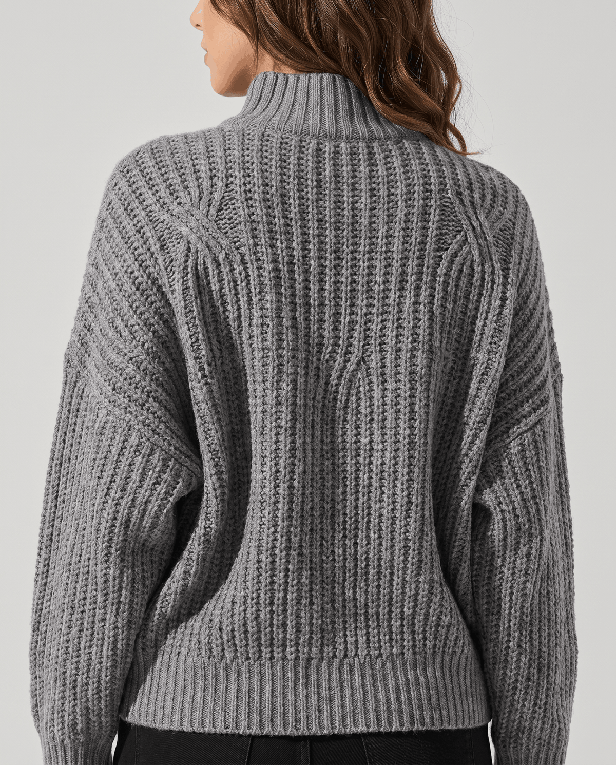 Gray Chunky Cable Knit Sweater worn by a female model from the back, highlighting the chunky cable knit texture, mock neck, relaxed fit, and ribbed hem.