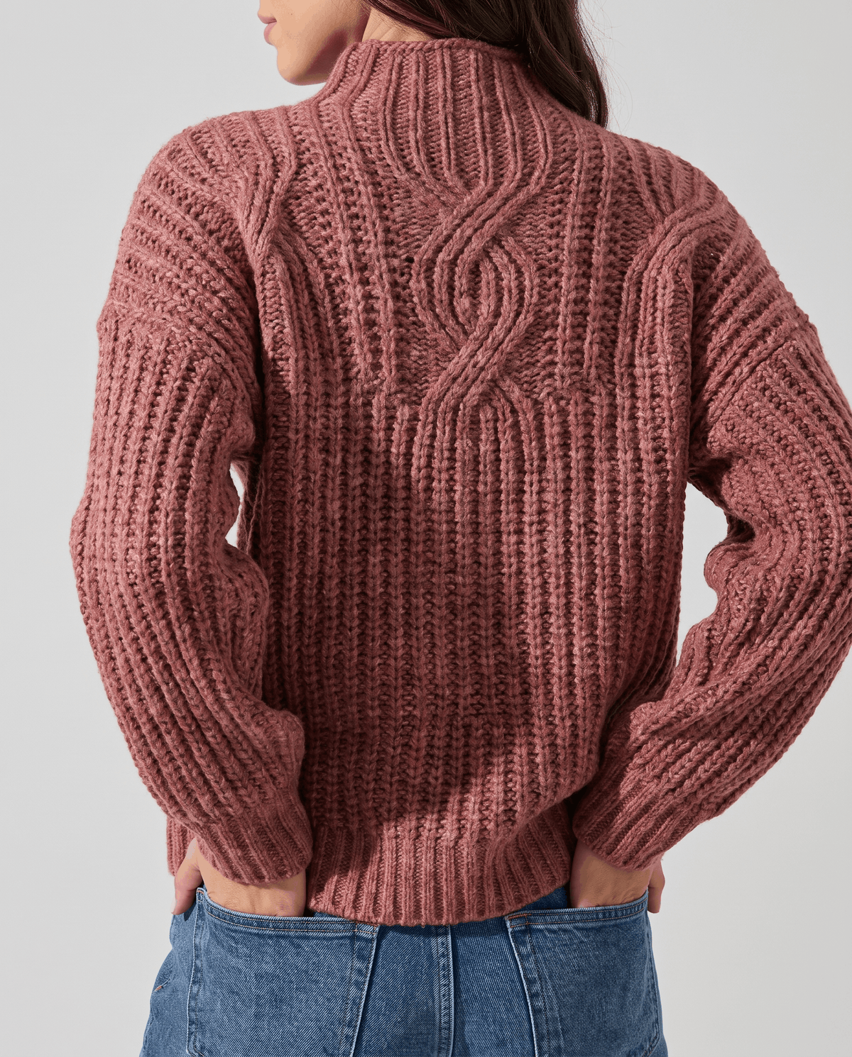 Pink Chunky Cable Knit Sweater worn by a female model from the back, highlighting the textured cable knit pattern, mock neck, relaxed fit, and ribbed hem.