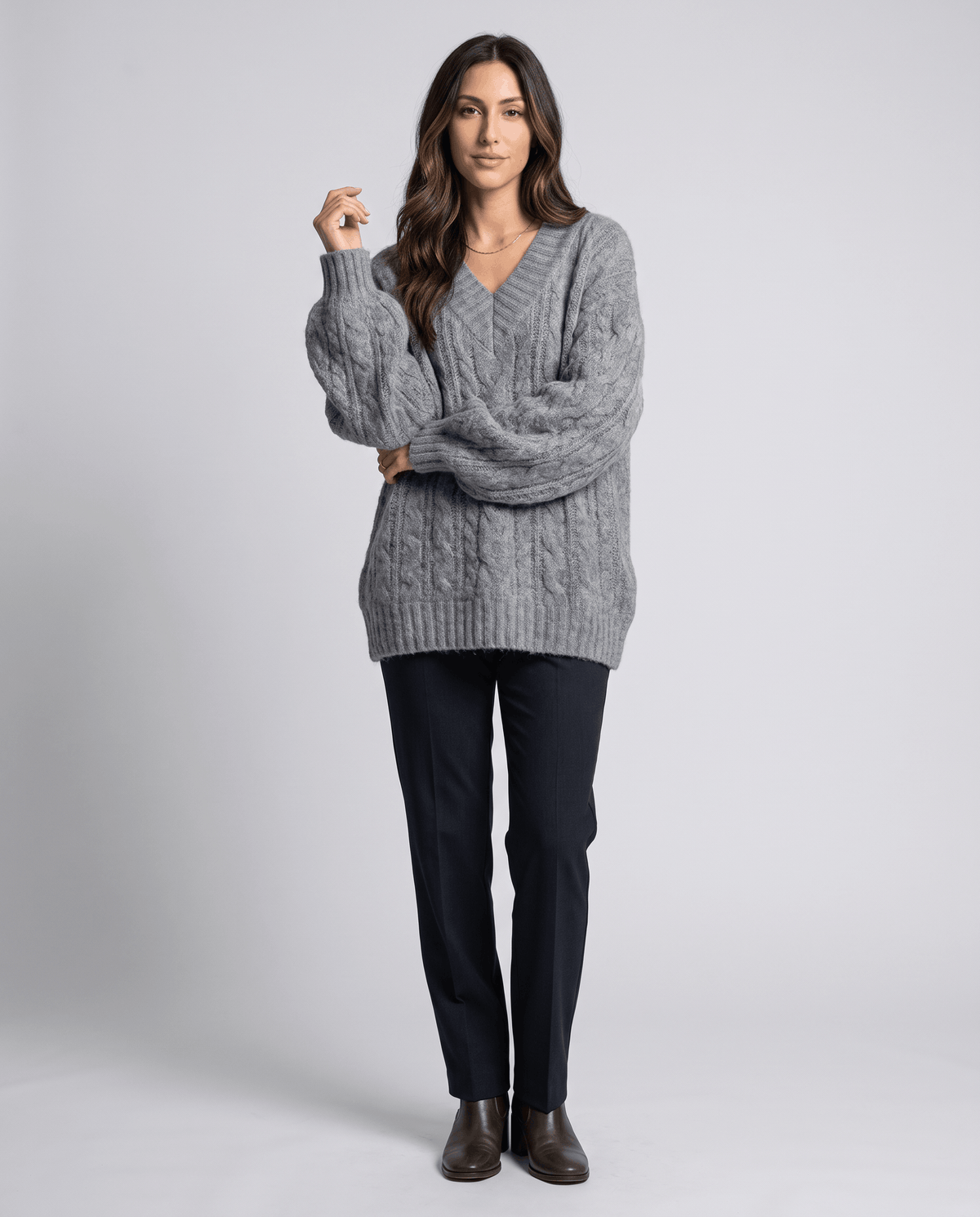Gray Chunky Cable Knit Sweater worn by a female model with dark pants and boots, featuring an oversized fit, textured cable knit pattern, V-neckline, and long sleeves.