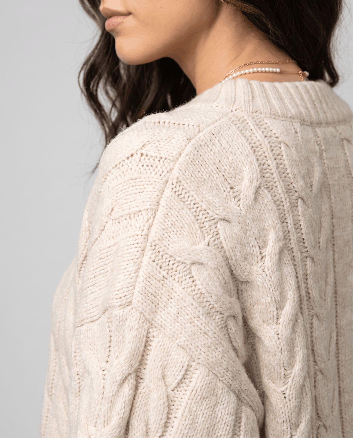 Cream Chunky Cable Knit Sweater –worn by a female model from the side, showcasing the textured cable knit pattern, relaxed oversized fit, and long sleeves.