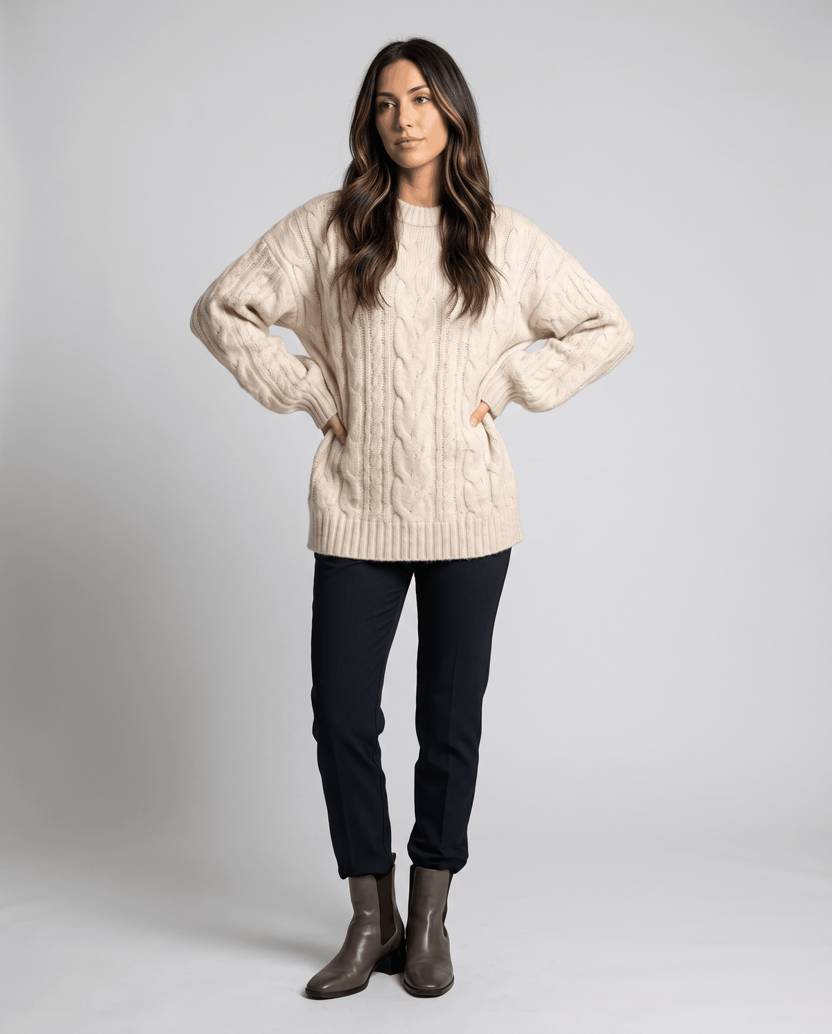 Cream Chunky Cable Knit Sweater worn by a female model with dark pants, featuring an oversized fit, textured cable knit pattern, long sleeves, and relaxed silhouette.